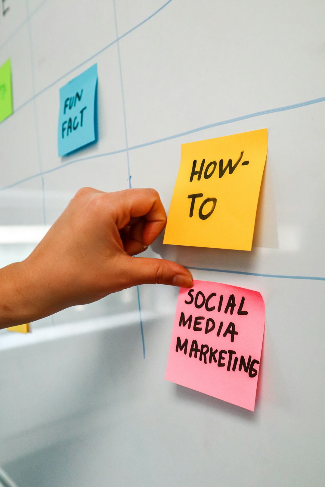 A person placing a sticky note onto a whiteboard with the words Social Media Marketing on it